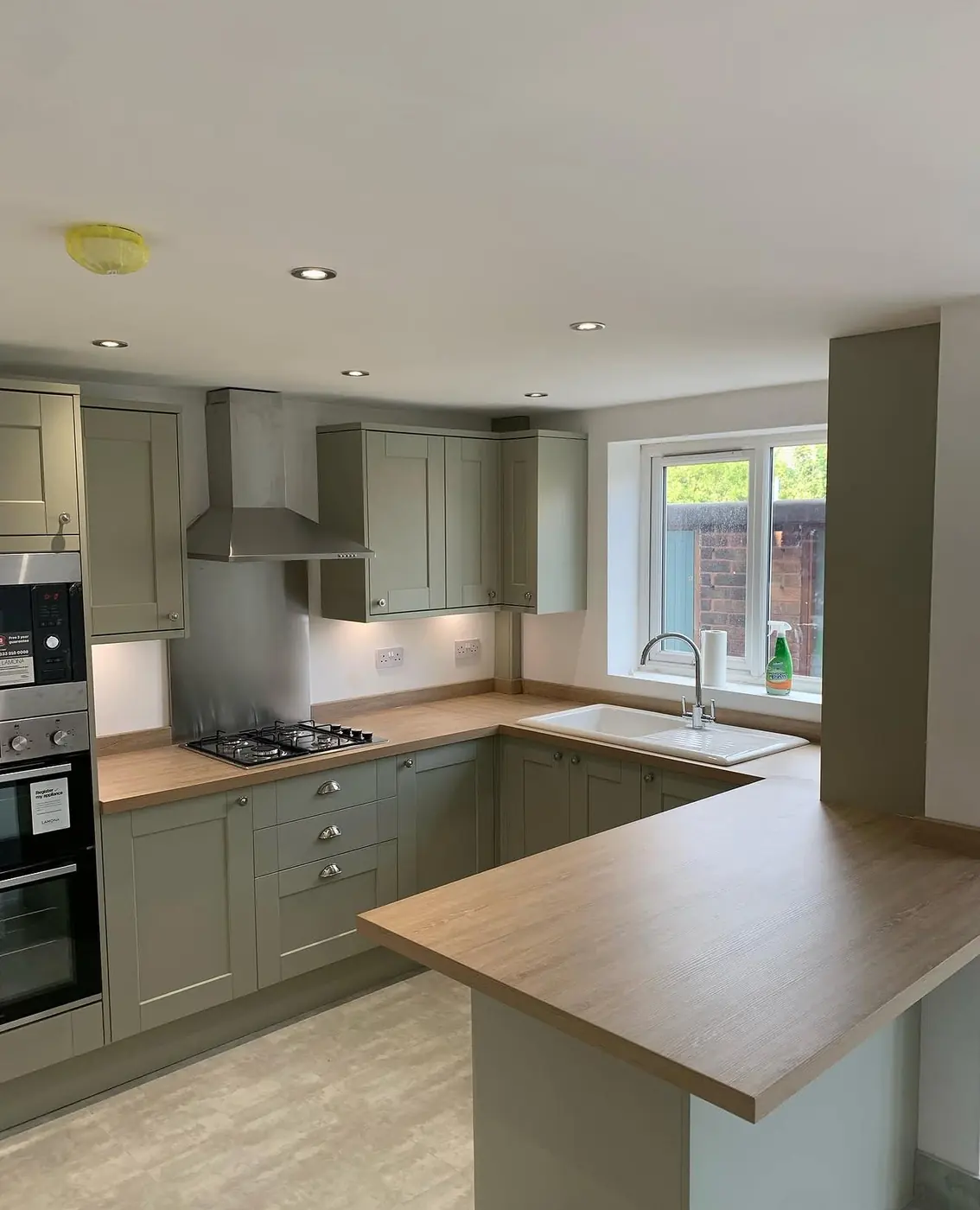 Sage green shaker kitchen with oak-effect worktop and integrated ovens
