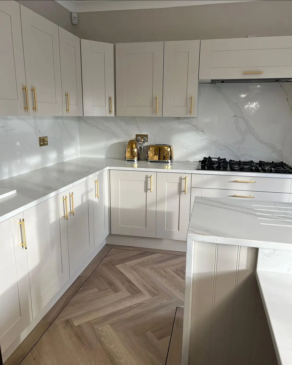 White shaker kitchen with gold handles and marble-effect splashback